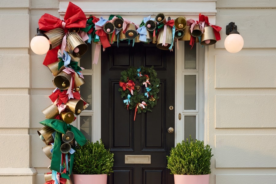 Porte d’entrée décorée d’une guirlande de cloches dorées et de rubans rouges et verts accrochée avec des crochets Command Outdoor, ainsi qu’une couronne suspendue à un crochet pour couronne Command.
