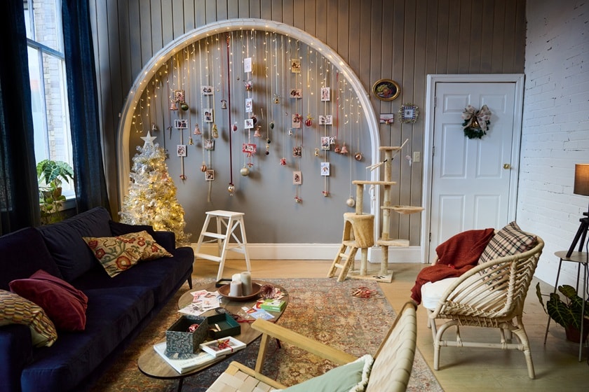 Salon avec des décorations de Noël suspendues à une arche à l’aide de crochets Command, un arbre blanc illuminé, un canapé sombre, une table basse centrale et un arbre à chat.
