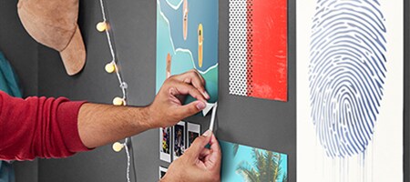 Un étudiant tire sur une Languette adhésive pour posters Command™ vers le bas afin de retirer un poster du mur de son logement étudiant

