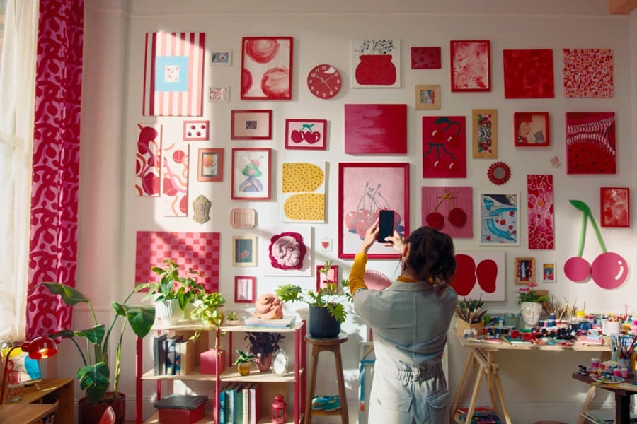 Salon avec des œuvres d’art sur le thème des cerises accrochées avec des bandes Command, ainsi qu’une étagère contenant des livres et des plantes et une table avec du matériel artistique.
